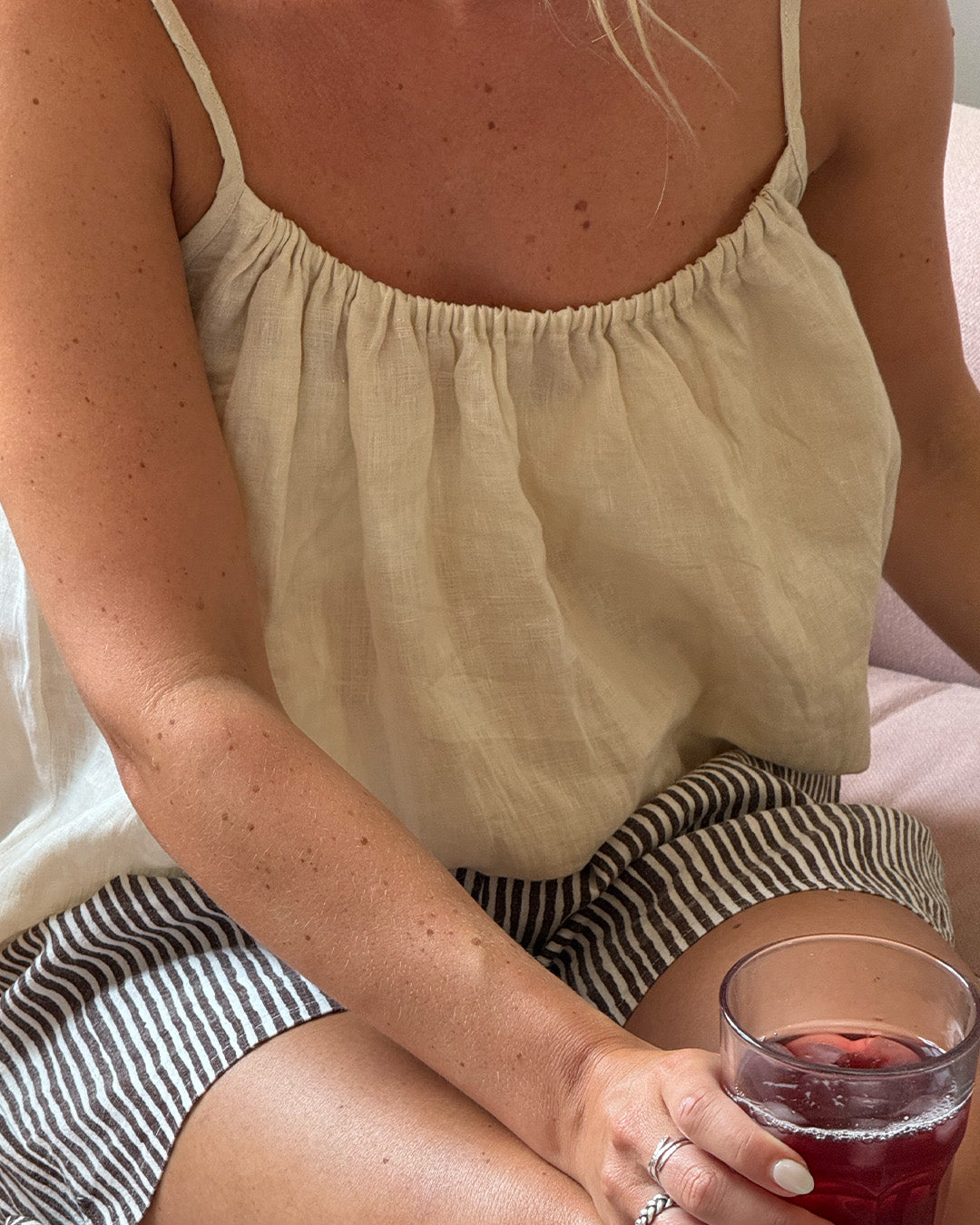 Person wearing a light-colored top and striped shorts, holding a glass of red wine.