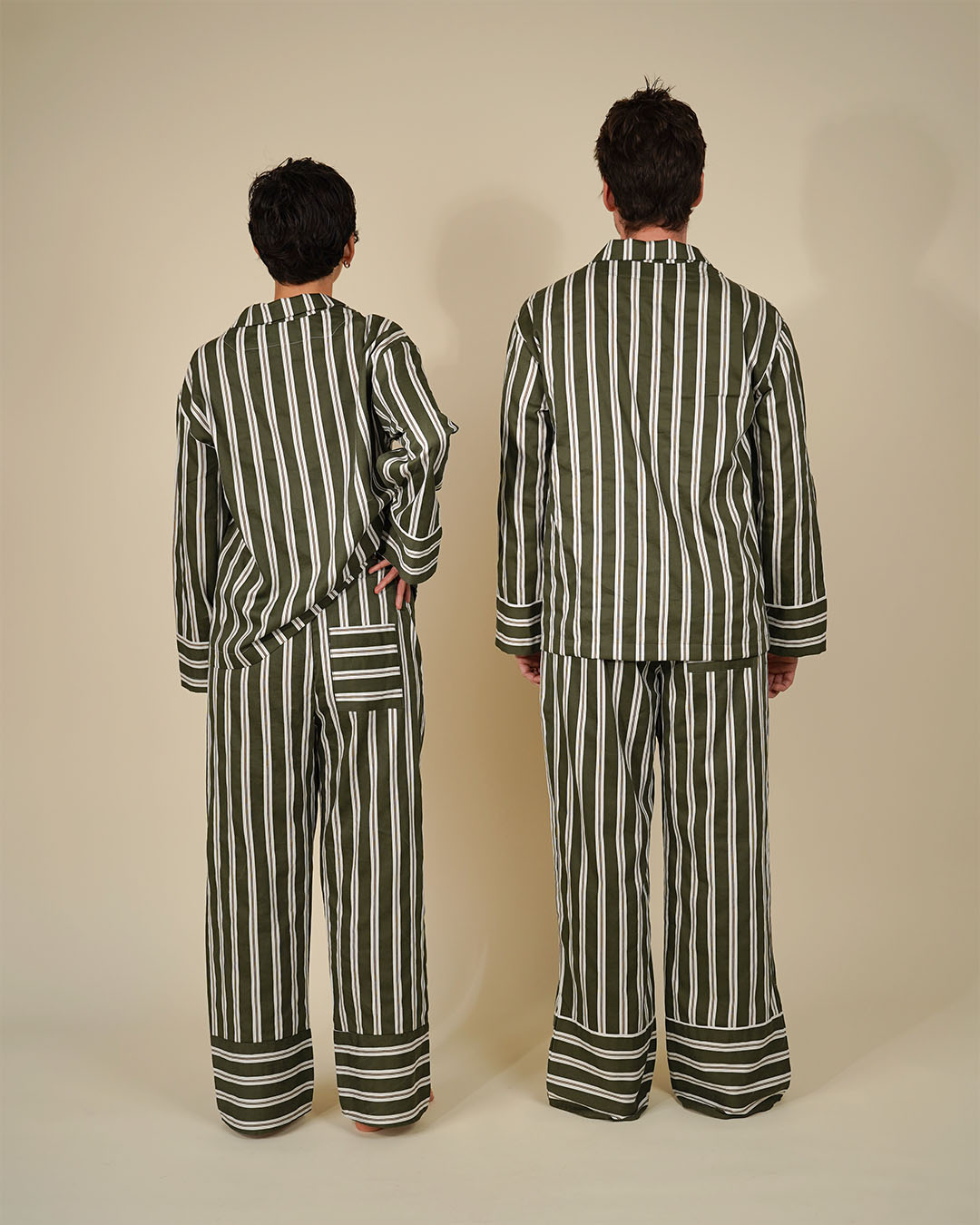 Two models shown from the back wearing matching striped pajama sets in olive green and white, standing against a plain beige studio background.